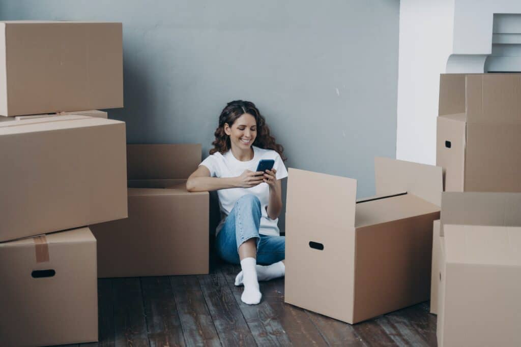 Happy girl choosing moving company for removal using phone sitting with boxes Mortgage relocation