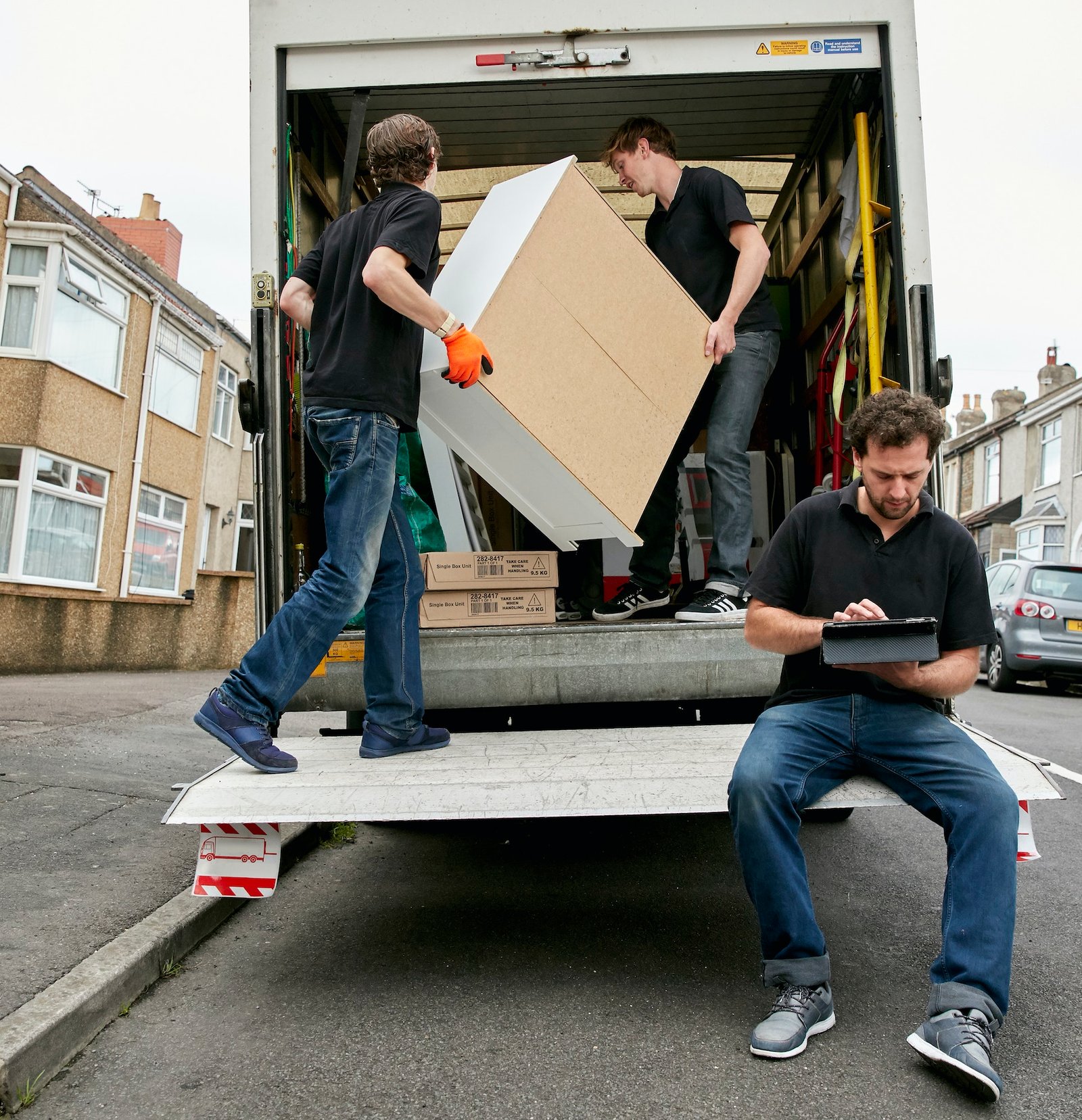Removals business. A removals company, two men lifting furniture and one seated using a digital